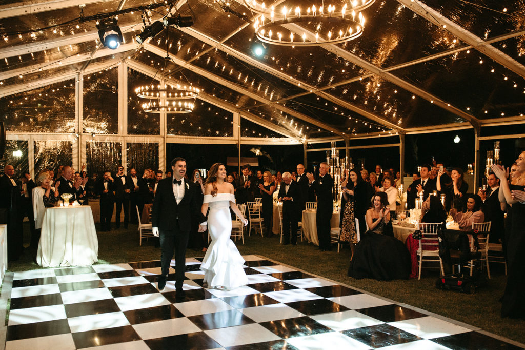 Wedding reception inside a clear top frame tent with checkered dance floor and chandelier lighting